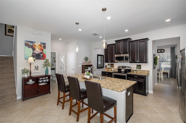 kitchen featuring appliances with stainless steel finishes, pendant lighting, sink, a kitchen bar, and a kitchen island with sink