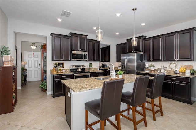 kitchen with a breakfast bar, sink, decorative light fixtures, appliances with stainless steel finishes, and an island with sink