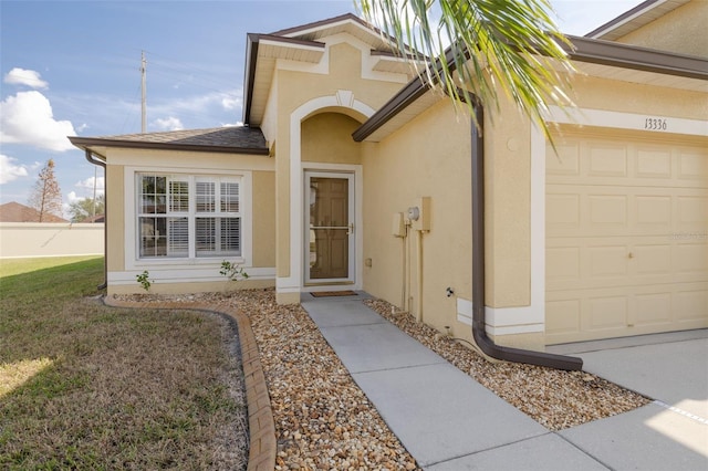 property entrance with a garage, a yard, roof with shingles, and stucco siding