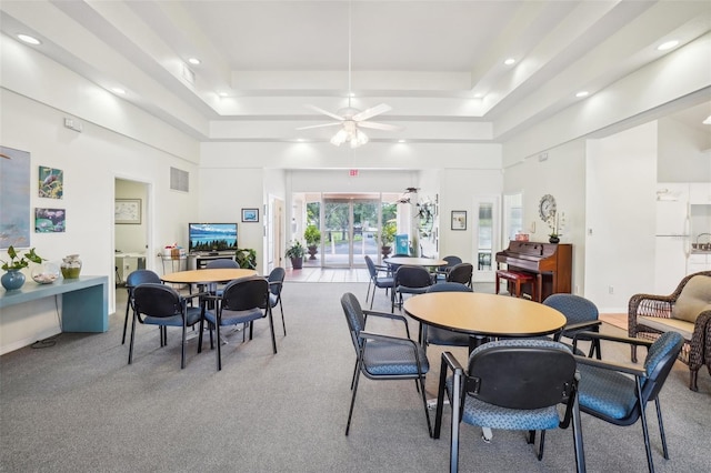 dining area featuring light carpet, a high ceiling, a tray ceiling, and ceiling fan