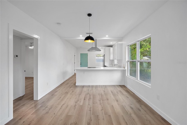 kitchen featuring kitchen peninsula, sink, light hardwood / wood-style flooring, decorative light fixtures, and white cabinetry