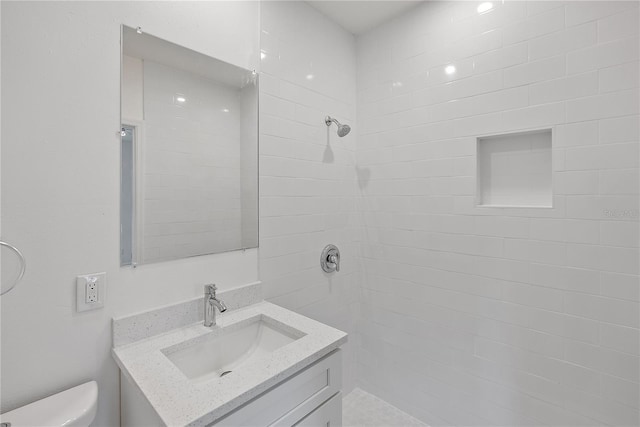 bathroom featuring a tile shower, vanity, and toilet