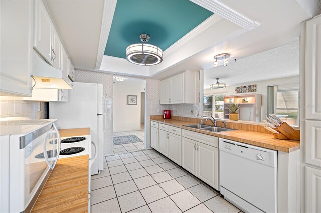 kitchen with white dishwasher, a raised ceiling, sink, decorative backsplash, and white cabinetry