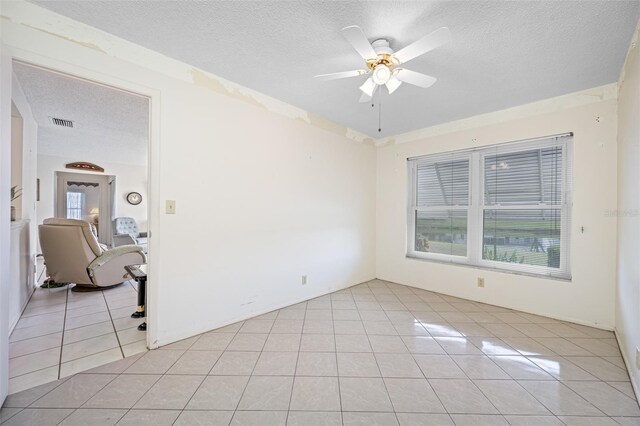 empty room featuring ceiling fan, light tile patterned floors, and a textured ceiling