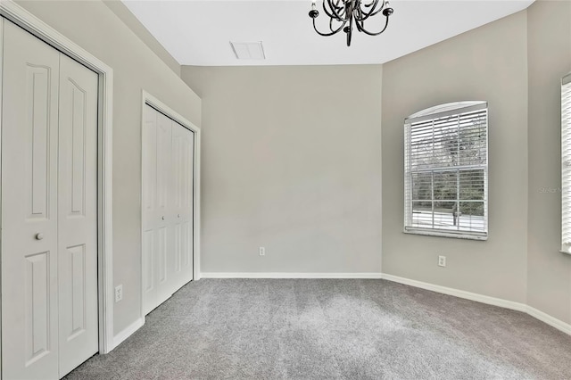 unfurnished bedroom featuring multiple closets, carpet floors, and a chandelier