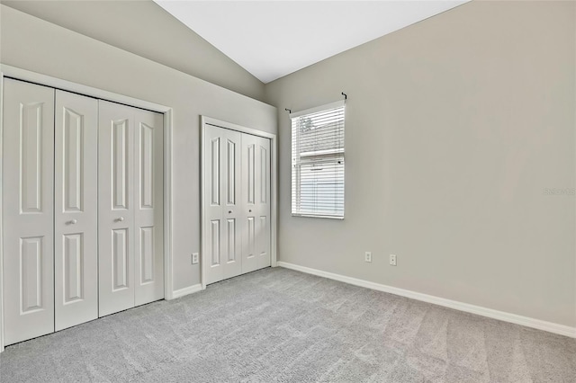 unfurnished bedroom with lofted ceiling, light colored carpet, and multiple closets