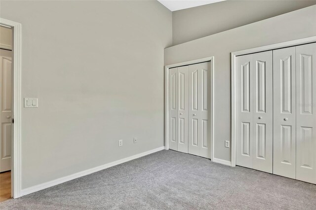 unfurnished bedroom featuring light colored carpet and multiple closets