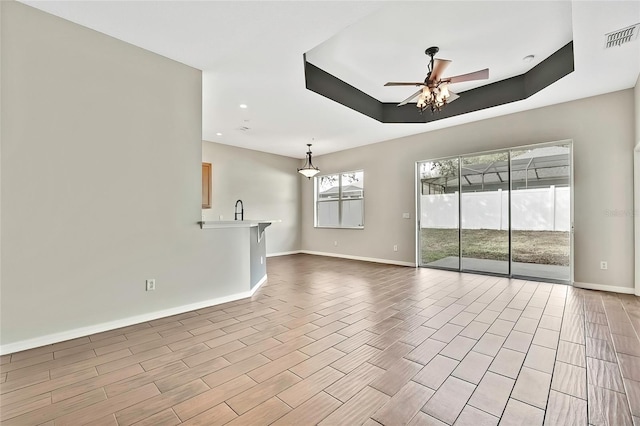 unfurnished living room with a raised ceiling, ceiling fan, sink, and light hardwood / wood-style floors