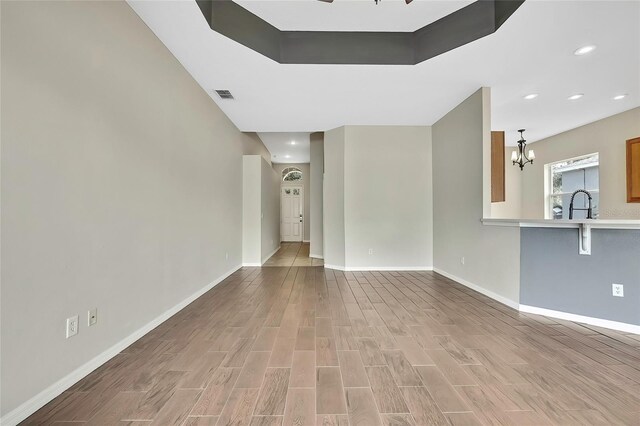 unfurnished living room featuring ceiling fan with notable chandelier, light hardwood / wood-style floors, and sink