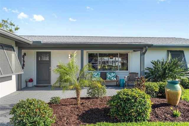property entrance with stucco siding, a shingled roof, and covered porch
