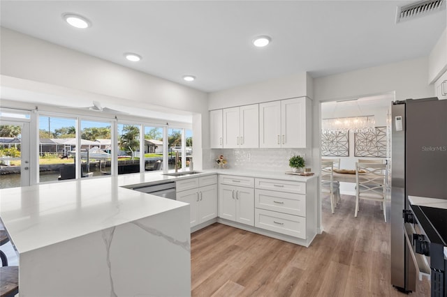 kitchen featuring visible vents, white cabinets, appliances with stainless steel finishes, a peninsula, and light stone counters