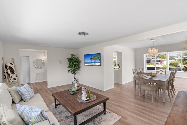 living area with light wood finished floors, visible vents, baseboards, and an inviting chandelier