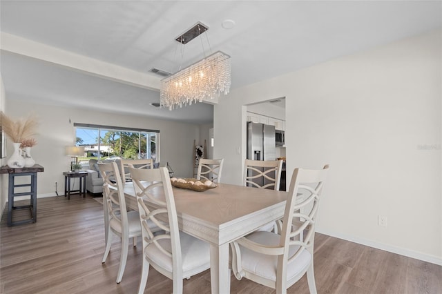 dining room with wood finished floors, an inviting chandelier, baseboards, and visible vents
