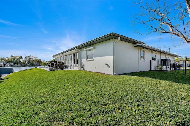 view of home's exterior with stucco siding, fence, a water view, and a lawn