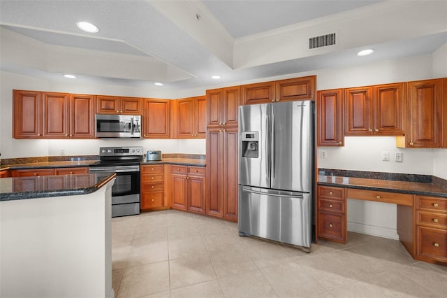 kitchen with a raised ceiling, crown molding, dark stone countertops, light tile patterned floors, and stainless steel appliances