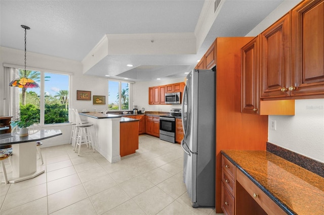 kitchen with hanging light fixtures, a tray ceiling, a breakfast bar, appliances with stainless steel finishes, and ornamental molding