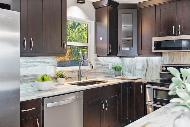 kitchen with dark brown cabinetry, light stone countertops, sink, decorative backsplash, and appliances with stainless steel finishes