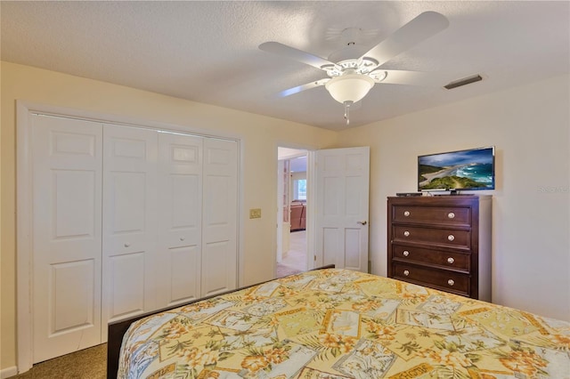 carpeted bedroom with ceiling fan, a closet, and a textured ceiling