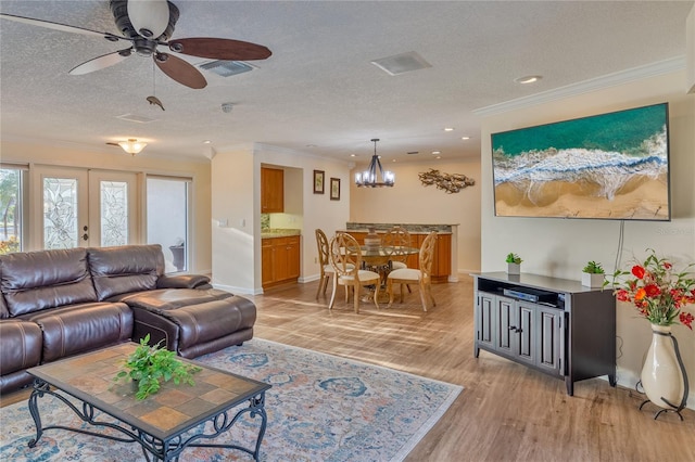 living room featuring light wood-type flooring, a textured ceiling, ceiling fan with notable chandelier, and ornamental molding