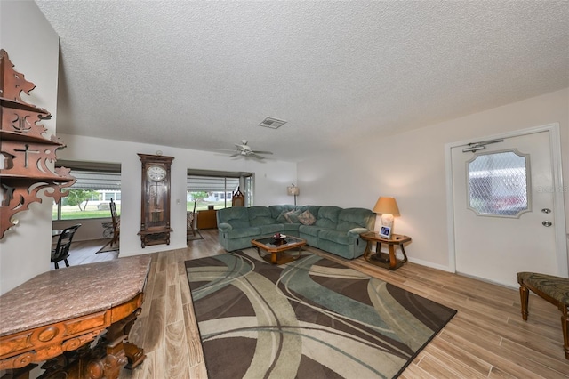 living room featuring ceiling fan, light hardwood / wood-style floors, and a textured ceiling