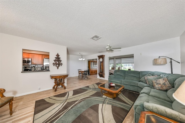 living room with ceiling fan with notable chandelier, light hardwood / wood-style floors, sink, and a textured ceiling