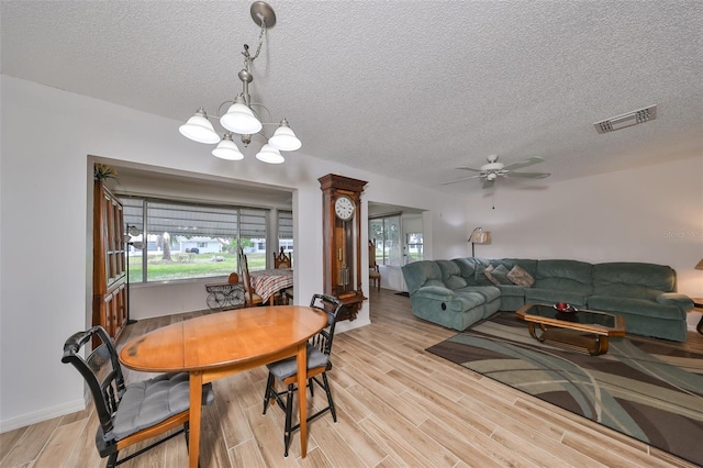 dining area with ceiling fan with notable chandelier, light hardwood / wood-style floors, and a textured ceiling