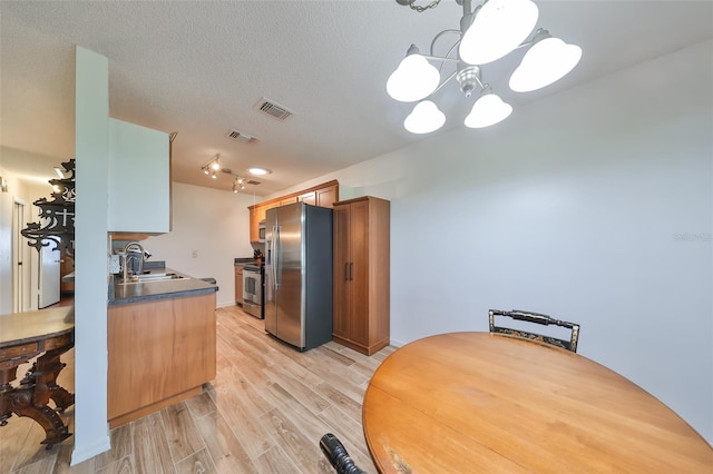 kitchen with a notable chandelier, light hardwood / wood-style floors, a textured ceiling, decorative light fixtures, and appliances with stainless steel finishes