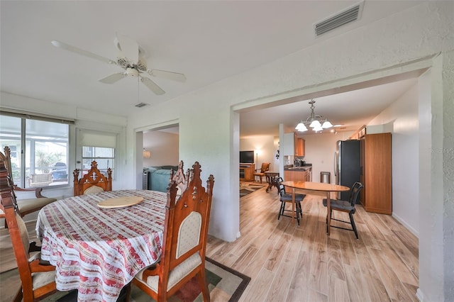 dining space with ceiling fan with notable chandelier and light hardwood / wood-style flooring