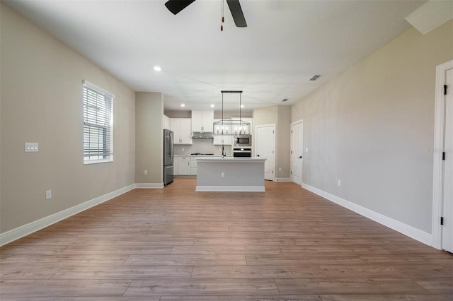 kitchen with stainless steel appliances, a kitchen island, hanging light fixtures, and light hardwood / wood-style flooring