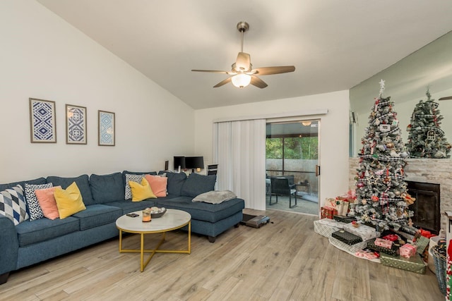 living room featuring a stone fireplace, ceiling fan, light hardwood / wood-style flooring, and lofted ceiling