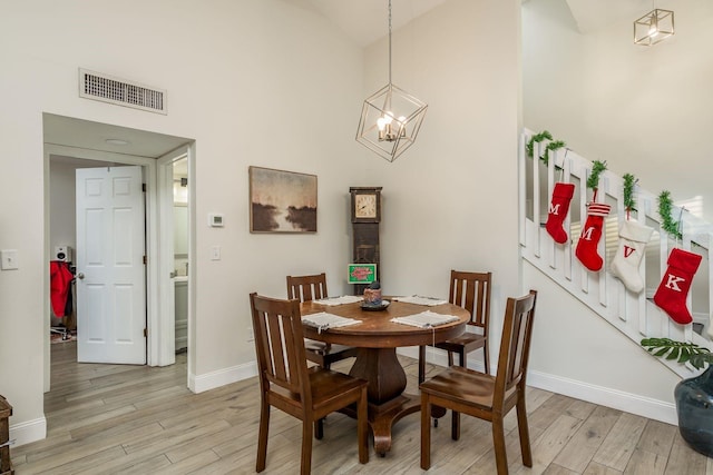 dining room with a towering ceiling, light wood-type flooring, and a notable chandelier