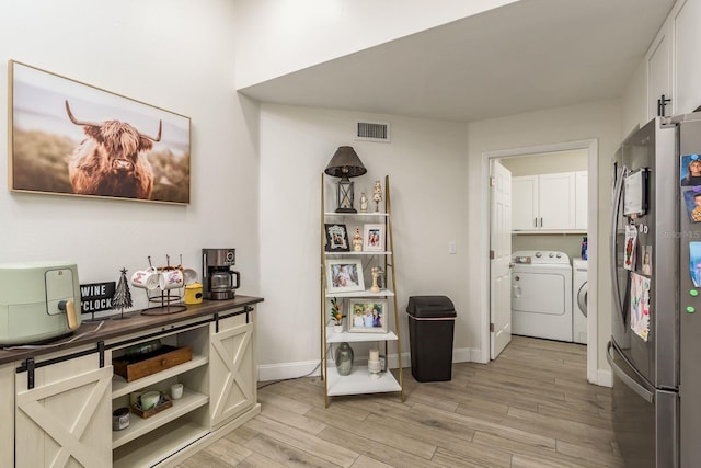 interior space with stainless steel refrigerator, white cabinetry, light wood-type flooring, and independent washer and dryer