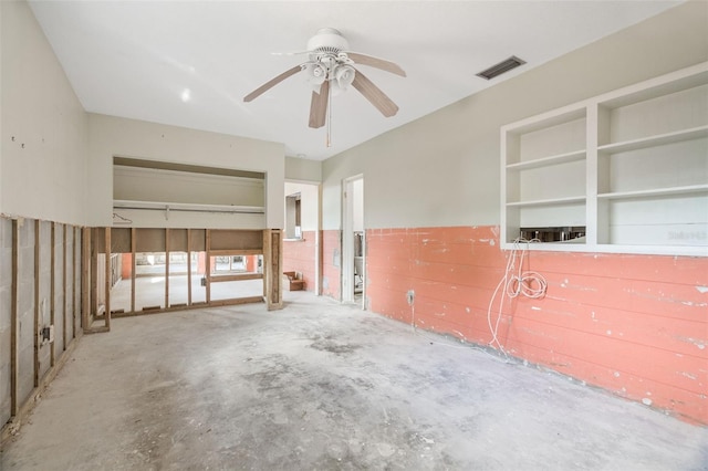 spare room featuring ceiling fan, concrete flooring, and built in shelves