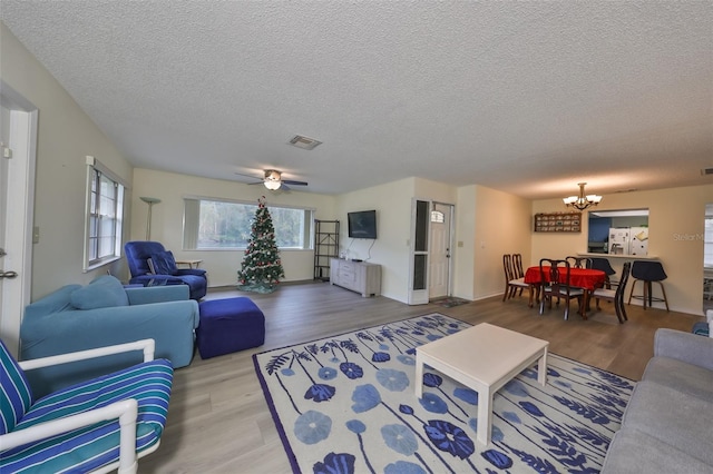 living room with ceiling fan with notable chandelier, wood-type flooring, and a textured ceiling