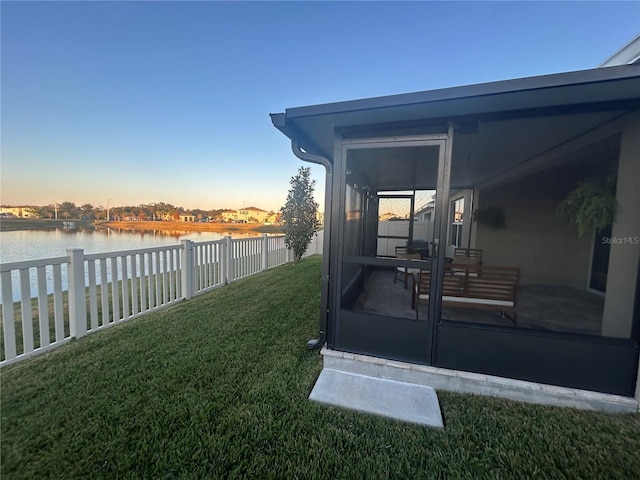 yard at dusk featuring a sunroom and a water view