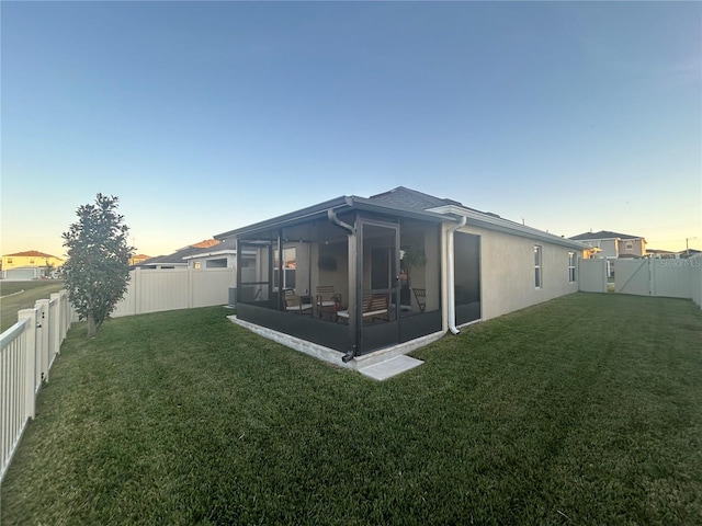 back house at dusk with a yard and a sunroom