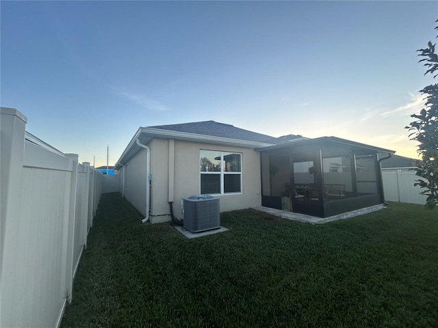 back house at dusk with a lawn, a sunroom, and cooling unit