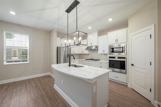 kitchen with white cabinetry, sink, stainless steel appliances, an island with sink, and decorative light fixtures