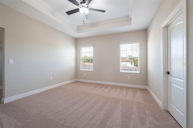 empty room with ceiling fan, a raised ceiling, light colored carpet, and ornamental molding