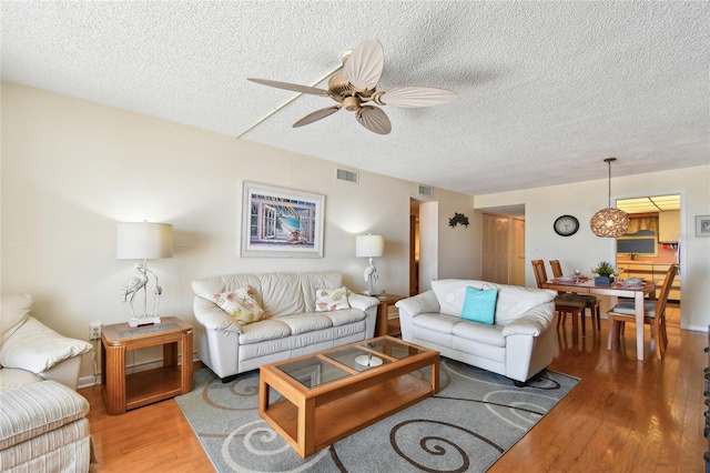 living room with hardwood / wood-style flooring, ceiling fan, and a textured ceiling