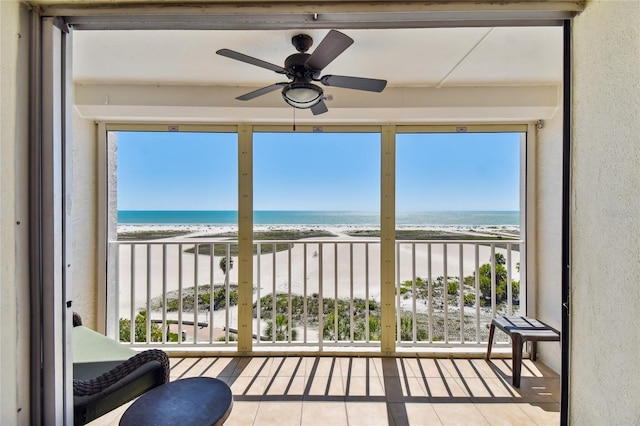 unfurnished sunroom featuring ceiling fan, a beach view, and a water view