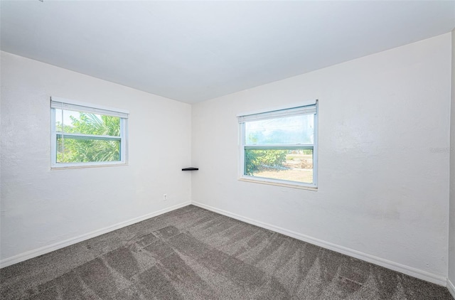 spare room featuring a healthy amount of sunlight and dark colored carpet