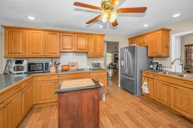 kitchen featuring stainless steel appliances, a center island, sink, backsplash, and ceiling fan