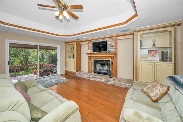 living room with a tray ceiling, ceiling fan, wood-type flooring, and a fireplace