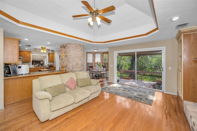 living room with light wood-type flooring, plenty of natural light, a tray ceiling, and ceiling fan