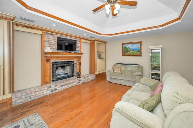 living room featuring light hardwood / wood-style flooring, ceiling fan, a fireplace, a tray ceiling, and ornamental molding