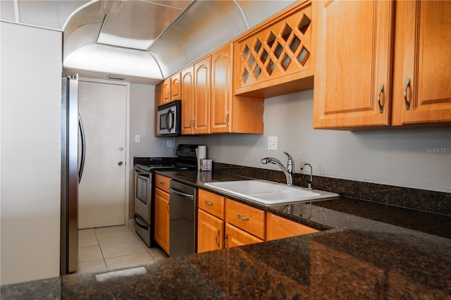 kitchen featuring appliances with stainless steel finishes, light tile patterned floors, dark stone countertops, and sink