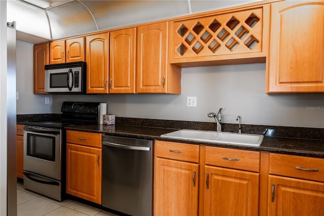 kitchen with light tile patterned flooring, stainless steel appliances, dark stone counters, and sink