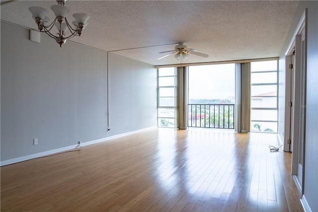 empty room with light hardwood / wood-style flooring, ceiling fan with notable chandelier, a textured ceiling, and a wall of windows