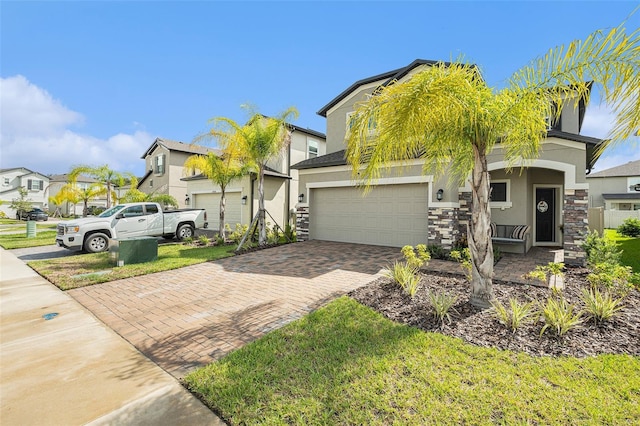 view of front of house featuring decorative driveway, stucco siding, an attached garage, a residential view, and stone siding